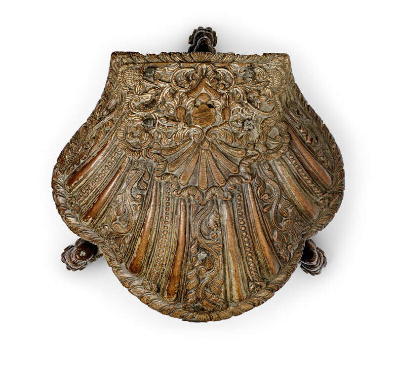 Ornate wooden box in the shape of a shell with detailed carvings, metal lock, and three small feet shaped like mythical creatures, photographed from the top on a white background.