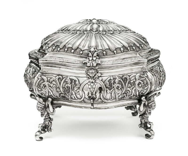 Ornate silver box in the shape of a shell, viewed head on, with hunting fingures on the base and mythical creatures serving as the feet and lock. Photographed on a white background.