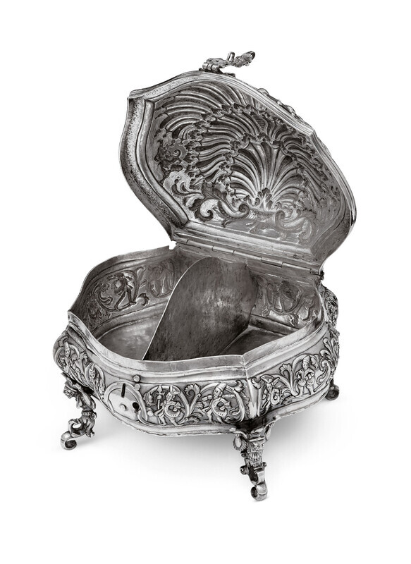Ornate silver box in the shape of a shell, viewed head on, with hunting fingures on the base and mythical creatures serving as the feet and lock. Box is open revealing two compartments separated by a thin silver wall. Photographed on a white background.