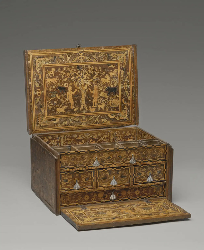 Wooden box with an open lid and fall front with ornate wooden inlay decor with general floral decor. The interior of the lid depicts a scene of a nude man and a nude woman in front of a tree that is circled by a snake. Photographed on neutral gray background