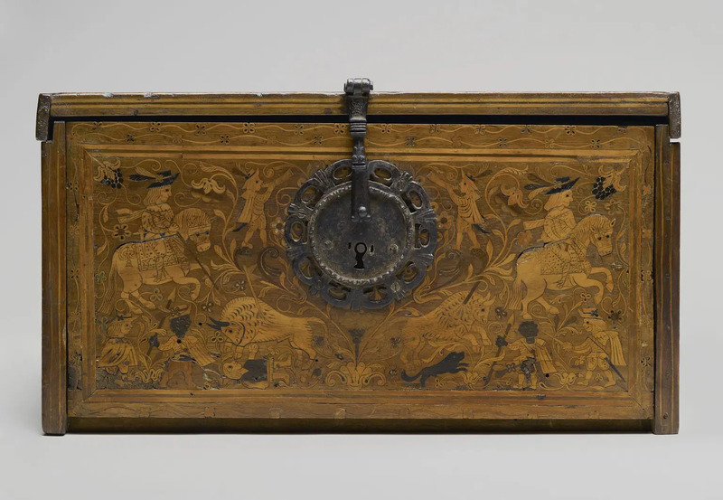 Detail of the front panel of the eooden box with ornate wooden inlay decor depicting a hunting scene with two men on horseback, two men with spears, two men with horns, and two bulls goring an additional two men laying down. Photographed on neutral gray background